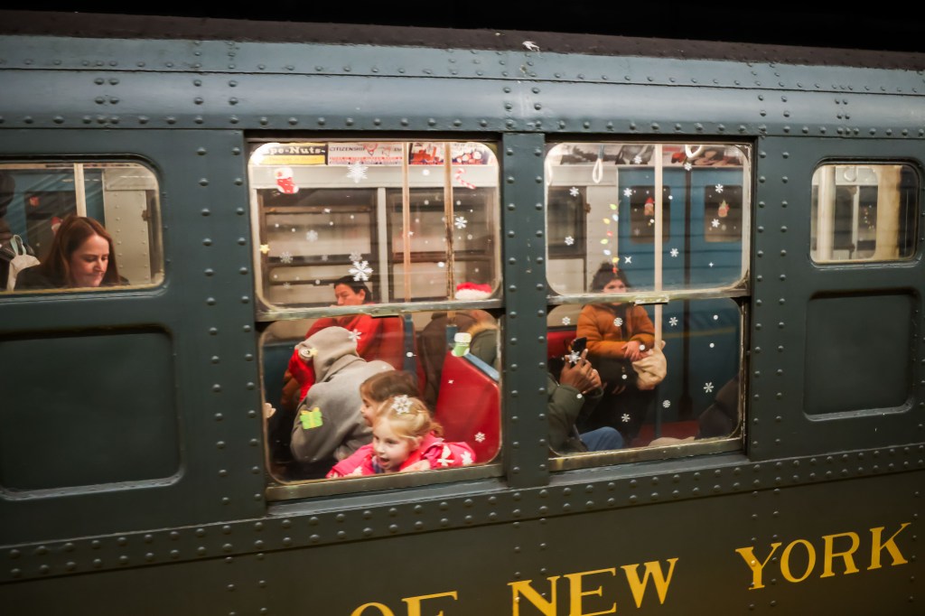 Passengers looking out of the windows of a holiday-decorated train car.