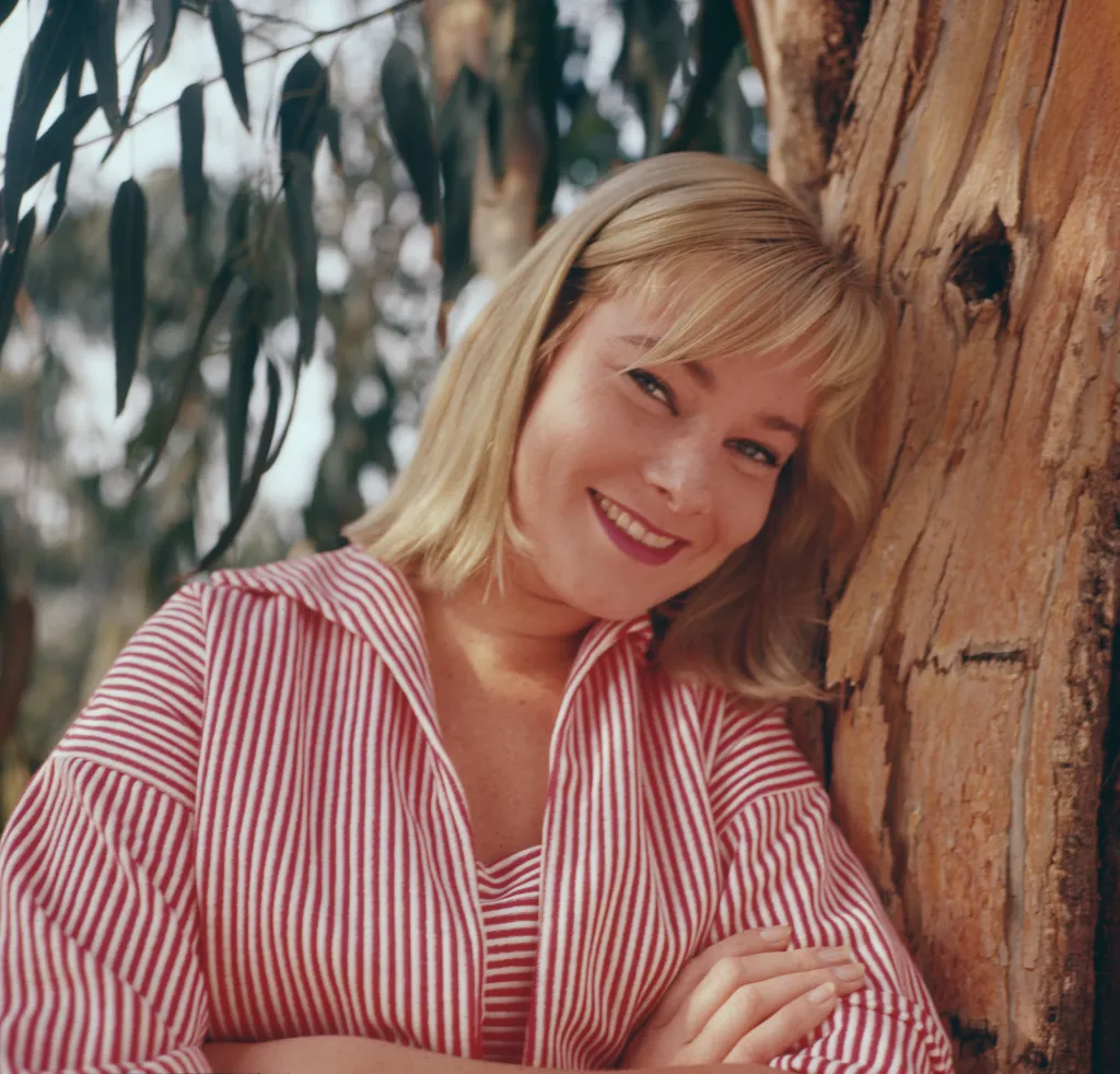 May Britt, Swedish actress and former wife of Sammy Davis Jr., smiling while leaning against a tree.