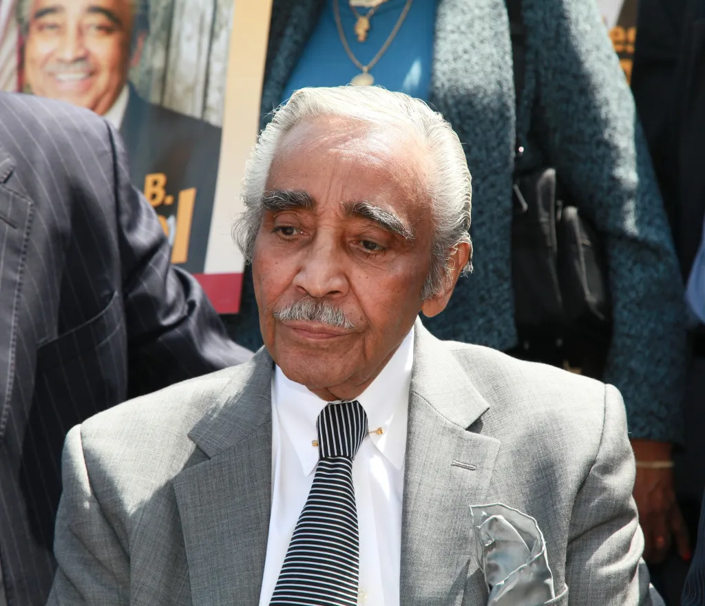 Charlie Rangel, a Black man with a gray mustache, wearing a gray suit and a black and white striped tie.