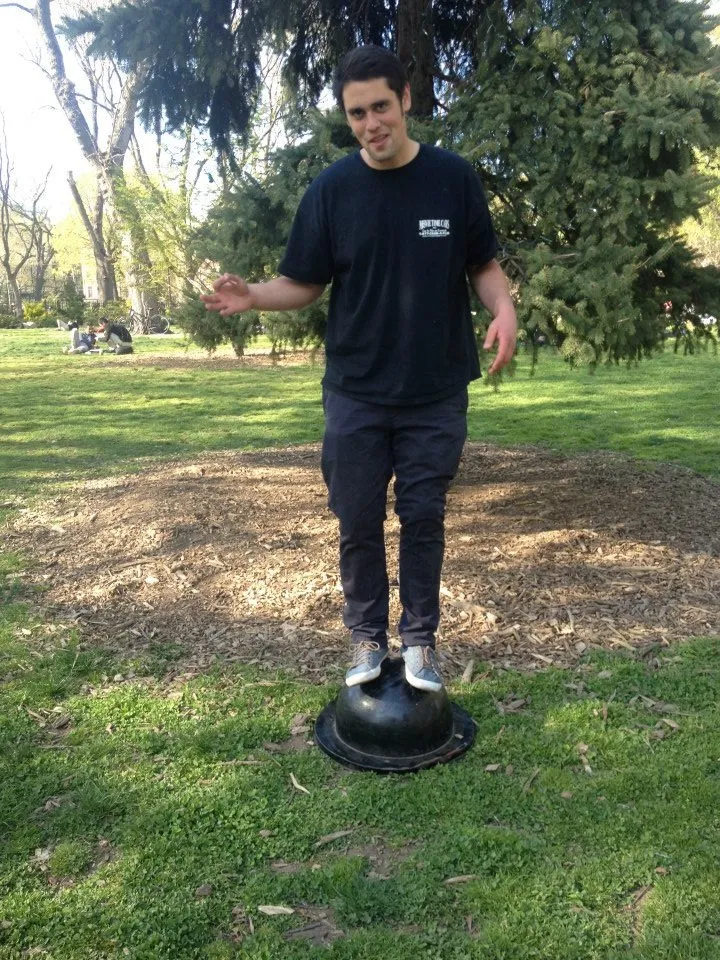 Nick Reiner standing on an upside-down black bowl in a park.