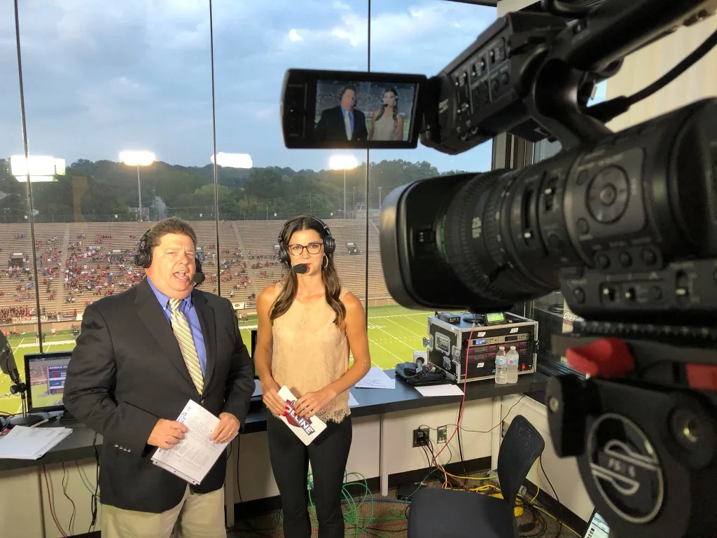 Christina Chambers and Rick Karle reporting on sports from a stadium booth.