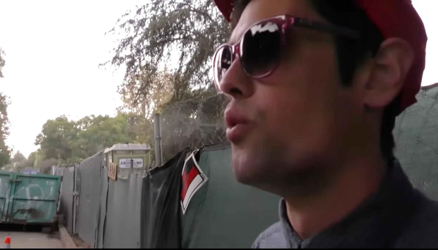 Nick Reiner in a red cap and sunglasses, with blurred trees and construction site in background.