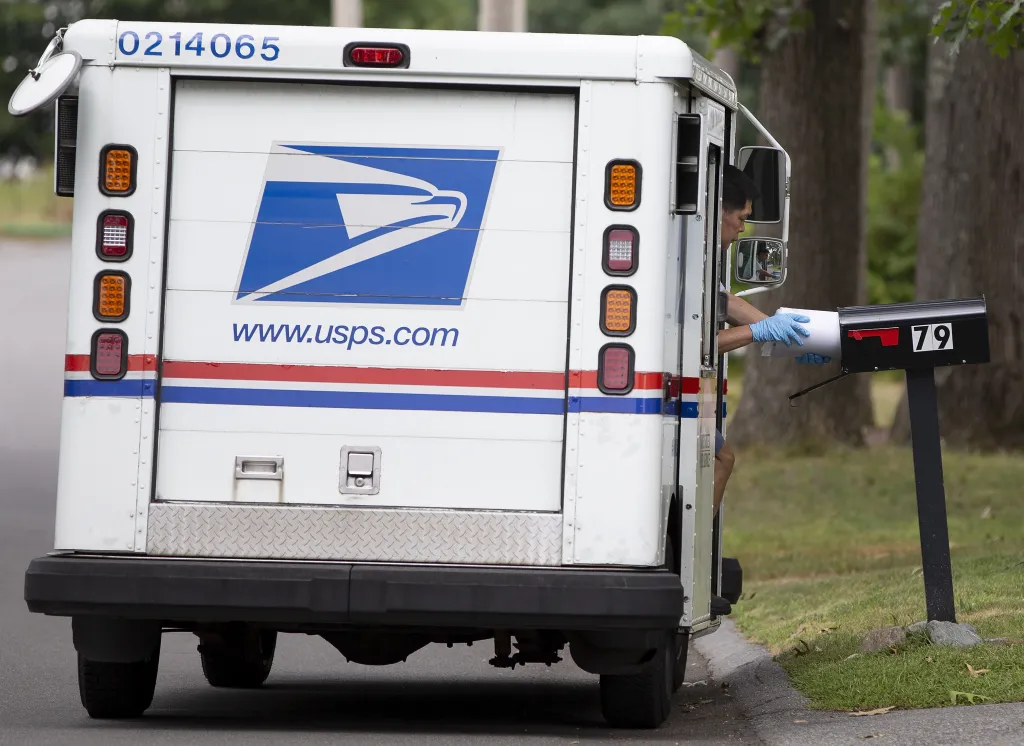 A USPS mail carrier inserts mail into a mailbox from their truck.