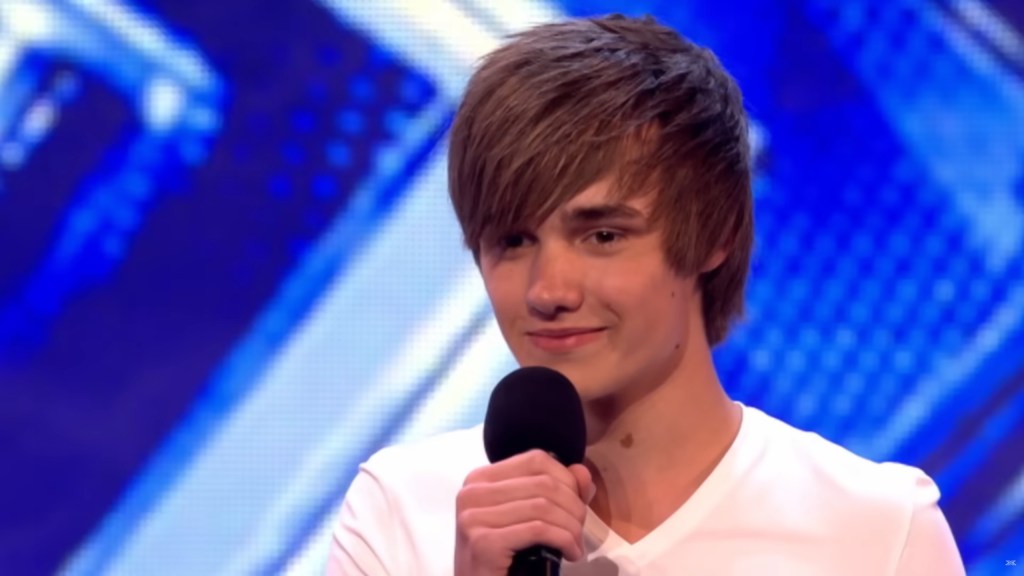 A 16-year-old Liam Payne in a white T-shirt, holding a microphone at his X Factor audition.