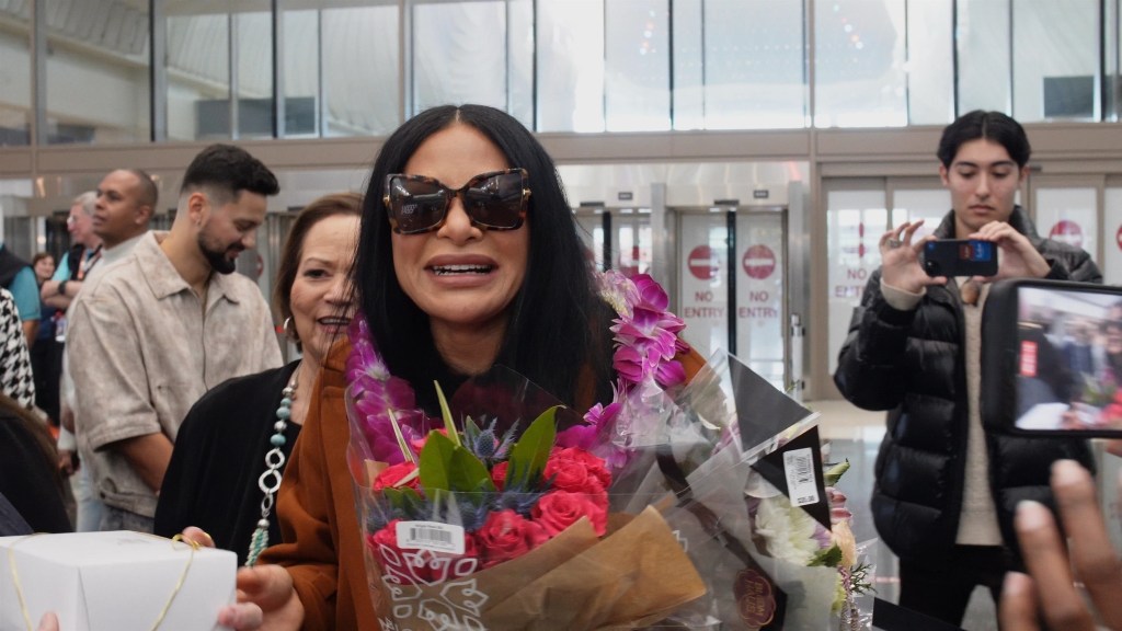 Jen Shah, wearing sunglasses and holding flowers, pictured for the first time since being released from jail, at Salt Lake City International Airport.