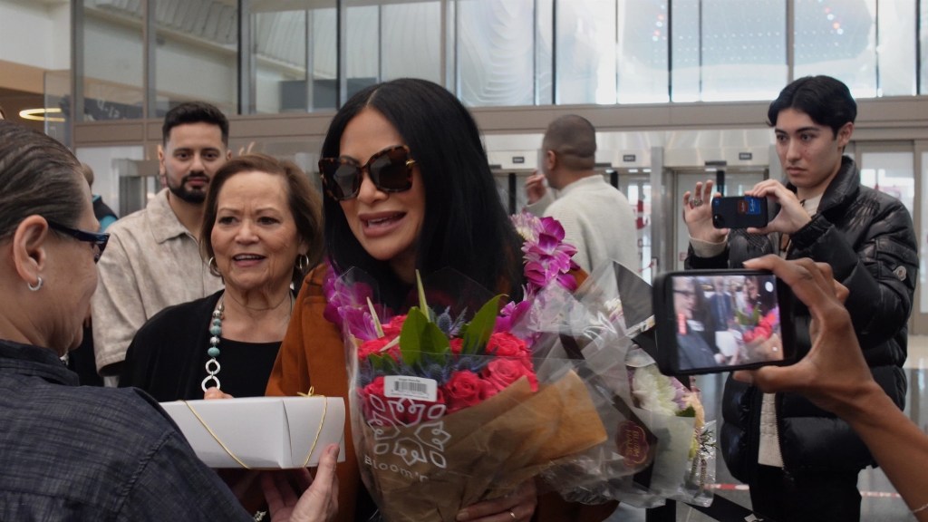 Jen Shah holding flowers and a gift box after her release from jail, surrounded by friends and family.