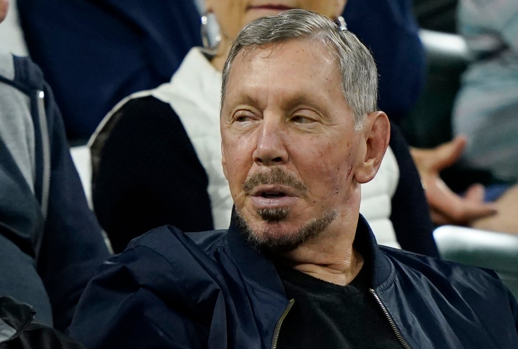Larry Ellison watches from the stands at a tennis tournament.