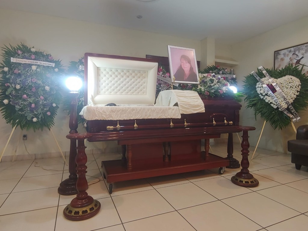 A casket surrounded by flower arrangements and a framed photo of Mirna Soza Arauz.