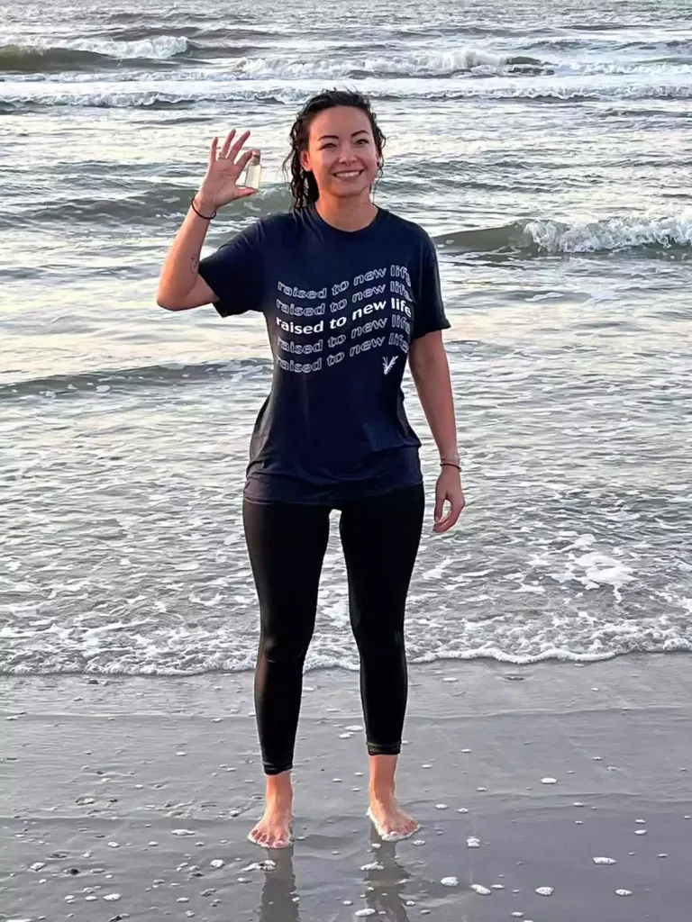 Mica Miller standing on a beach, holding a small bottle, with