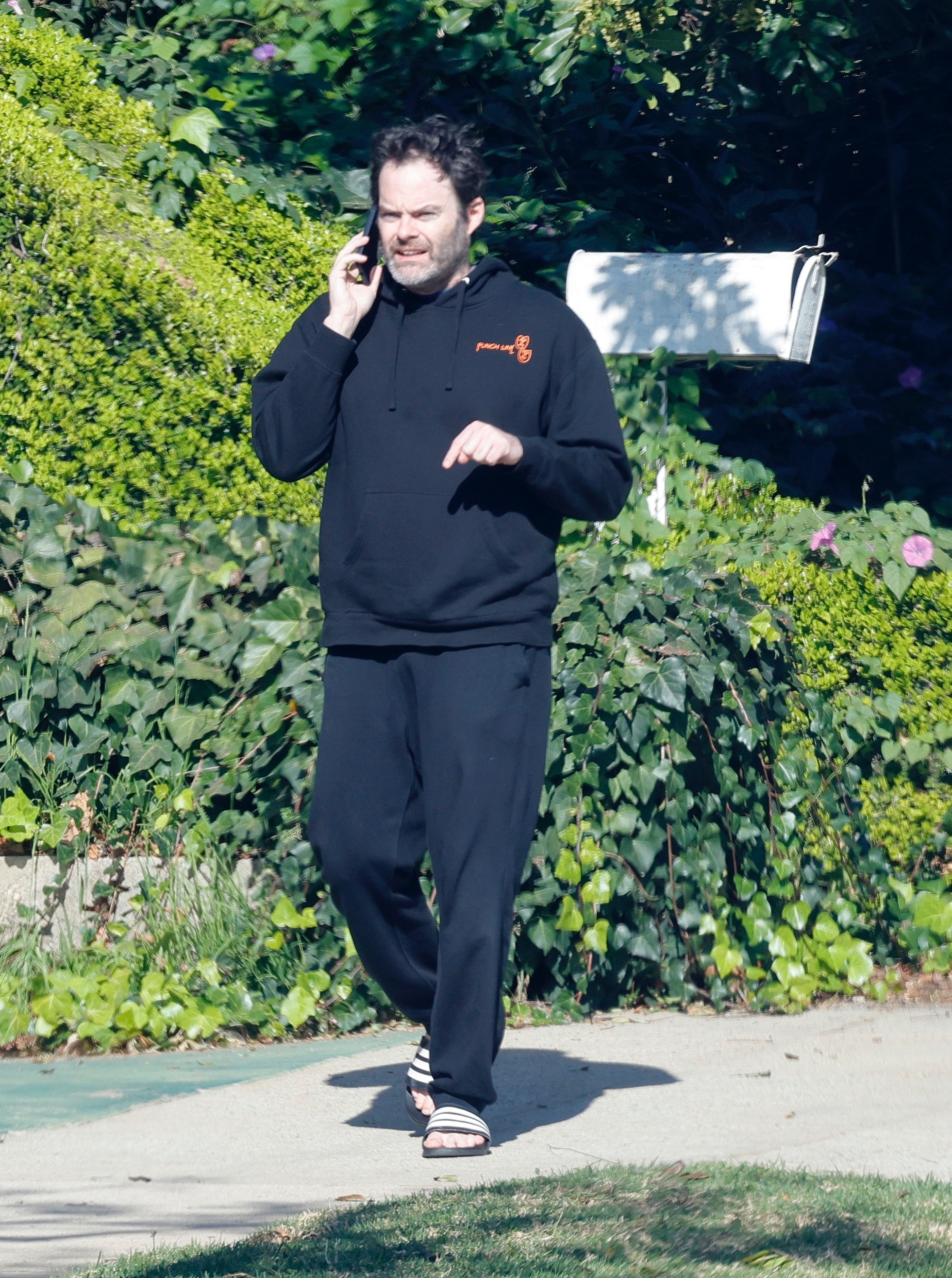 Bill Hader wearing a black hoodie and sweatpants while talking on a phone.