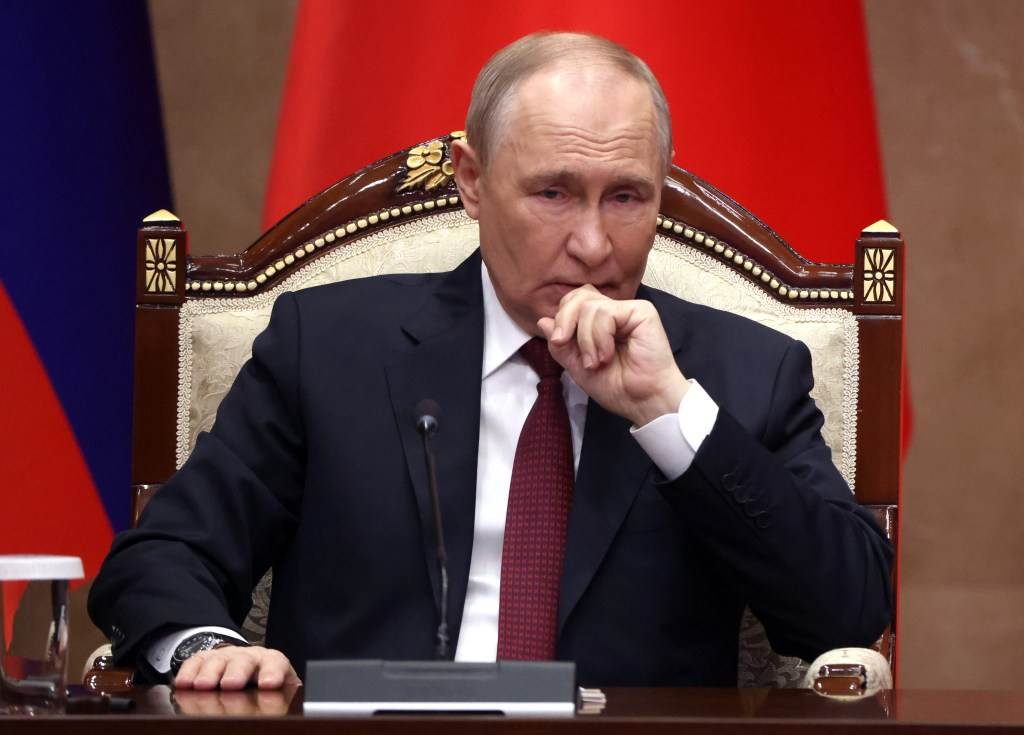 Russian President Vladimir Putin grimacing with his hand near his mouth.