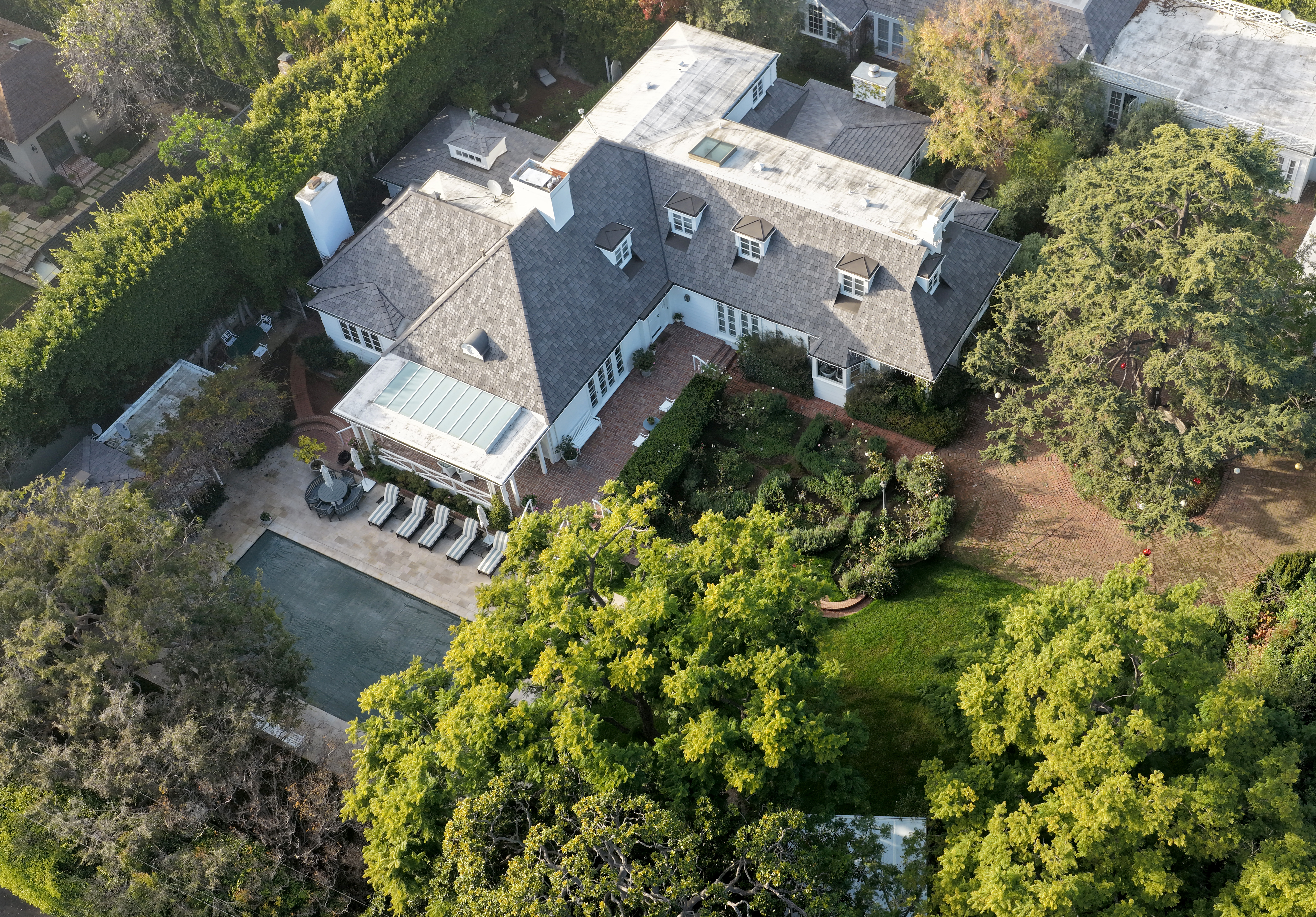Aerial view of Rob Reiner's Brentwood home, showing a large house with a gray roof, surrounded by green trees, with a swimming pool and patio area visible.