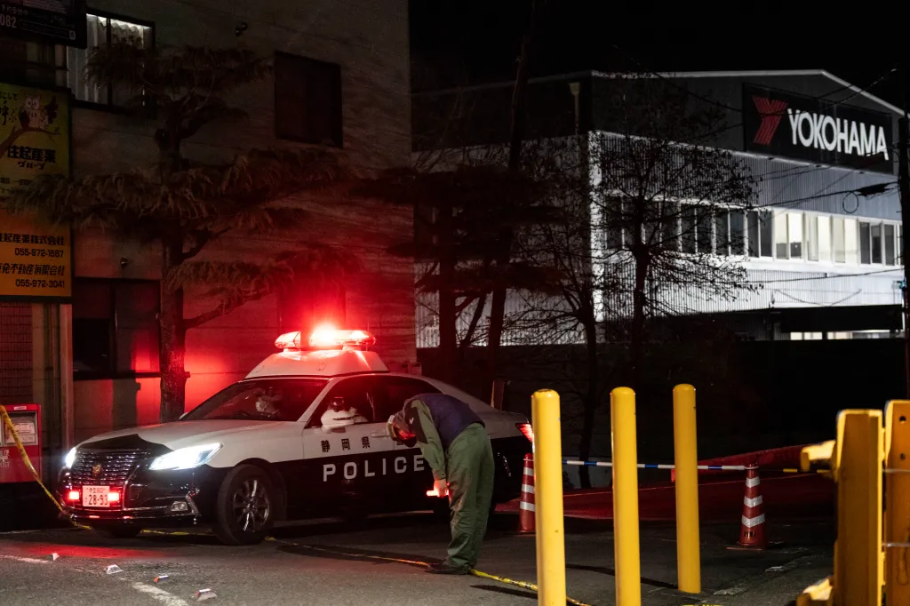 A worker bows as a police car leaves the Yokohama Rubber Mishima Plant after a stabbing attack.