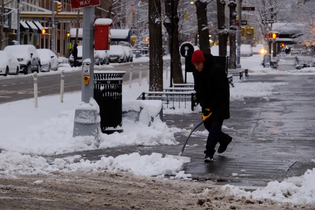 New Yorkers clear snow from the sidewalk on Fifth Avenue near Washington Square Park on Dec. 27, 2025.