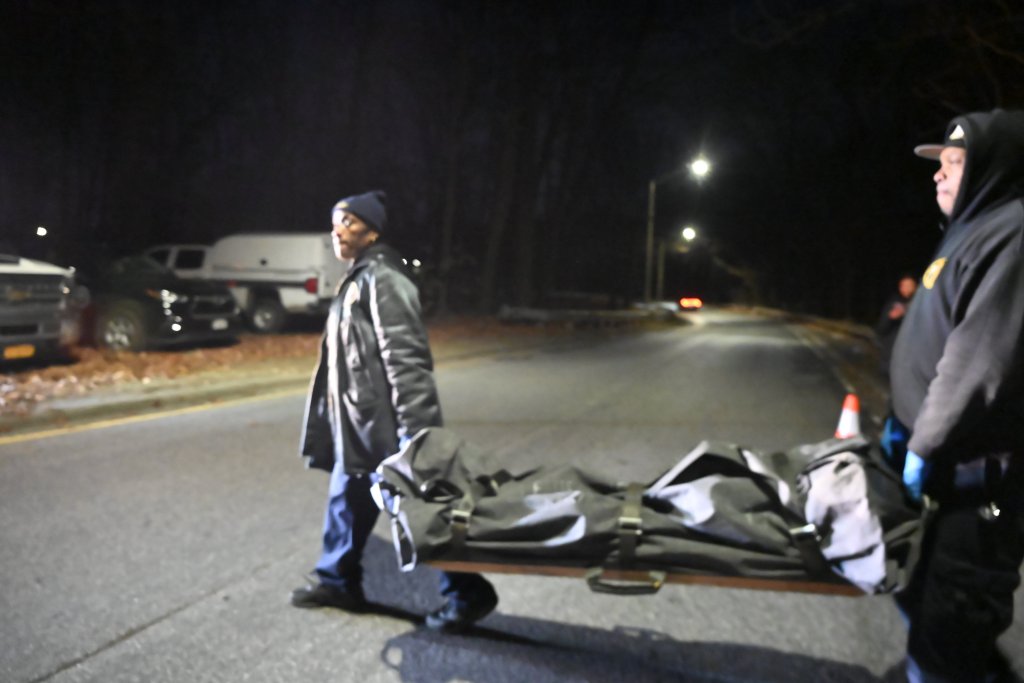 Police and medical examiner personnel removing human remains on a stretcher at night from the Major Deegan Expressway in the Bronx, New York.