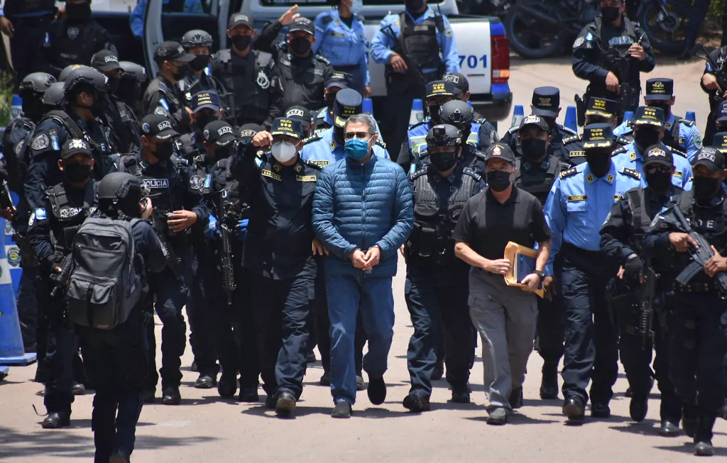 Former President Juan Orlando Hernandez (center, in blue jacket and jeans with handcuffs) is escorted by police officers.