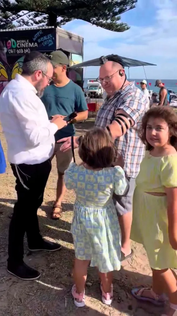 10-year-old Matilda, the youngest victim of a mass shooting at Australia's Bondi Beach targeting an event for the Jewish festival of Hanukkah on Sunday, looks on as Rabbi Eli Schlanger performs a Tefillin ritual in Sydney, Australia, December 14, 2025.
