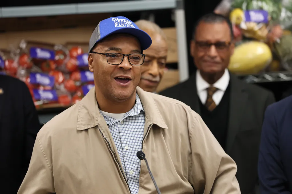 Assemblyman Eddie Gibbs speaking at a press conference, wearing a blue hat that says 