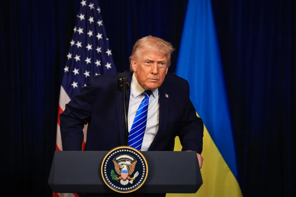 Donald Trump speaking at a podium with US and Ukrainian flags behind him.