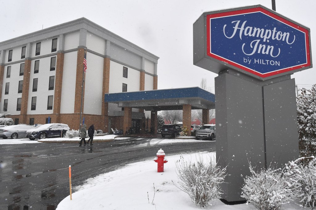Passers-by walk toward a Hampton Inn in Coventry, R.I., where a person of interest in a Brown University shooting was detained.