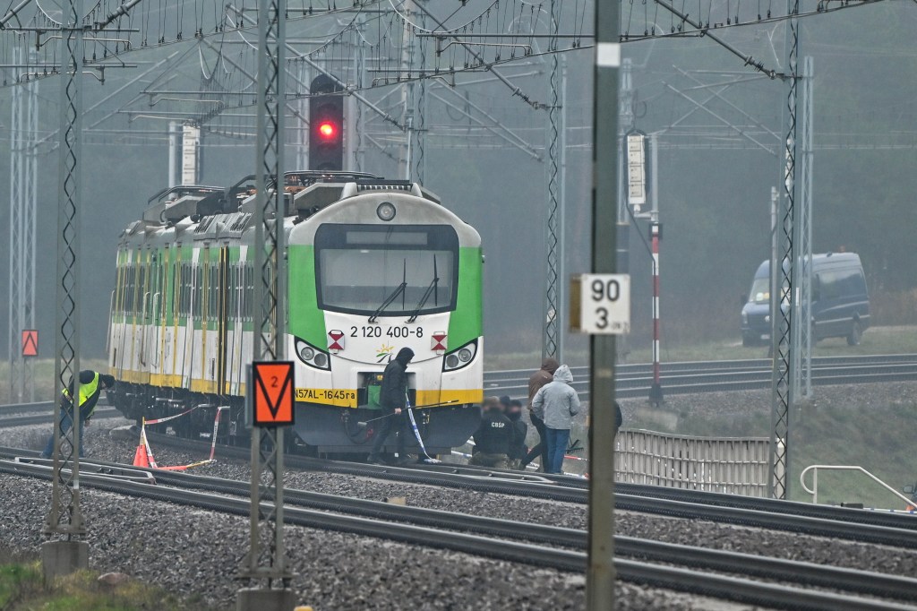 Green and white train stopped on tracks where an explosion occurred, with personnel investigating.