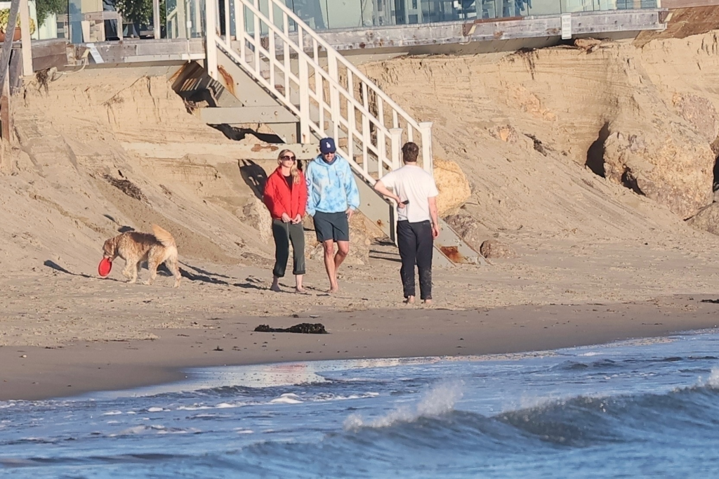 Jake Reiner, Maria Gilfillan, and Alex Silberberg walk on Malibu Beach with a dog.