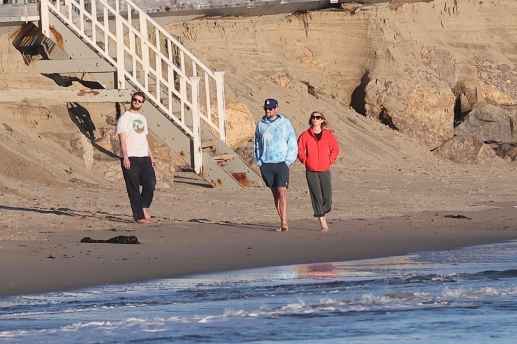 Jake Reiner, Maria Gilfillan, and Alex Silberberg walking on a sandy beach by the water.