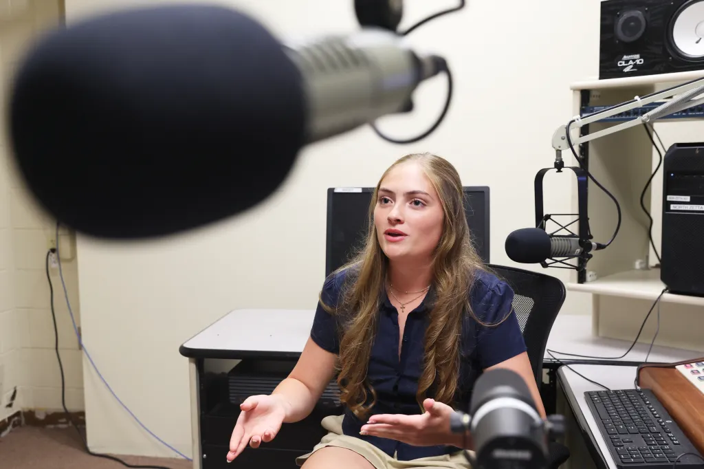 Alyssa Tappin in a radio studio at Sachem High School North, gesturing with her hands while speaking into a microphone.