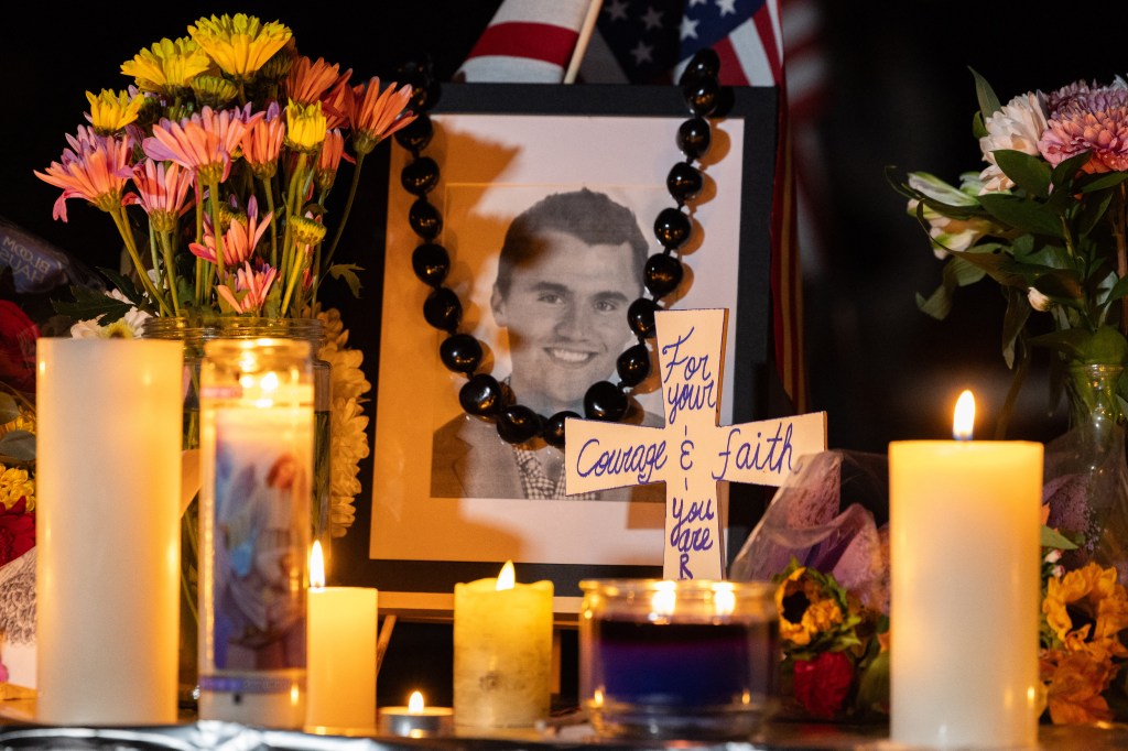 Candles and flowers around a portrait of Charlie Kirk at a memorial.