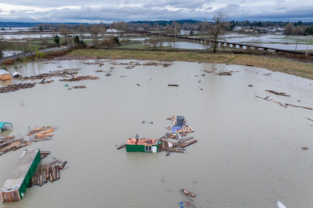 Aerial view of a person standing on the roof of a house surrounded by floodwater and debris in Snohomish, Washington.
