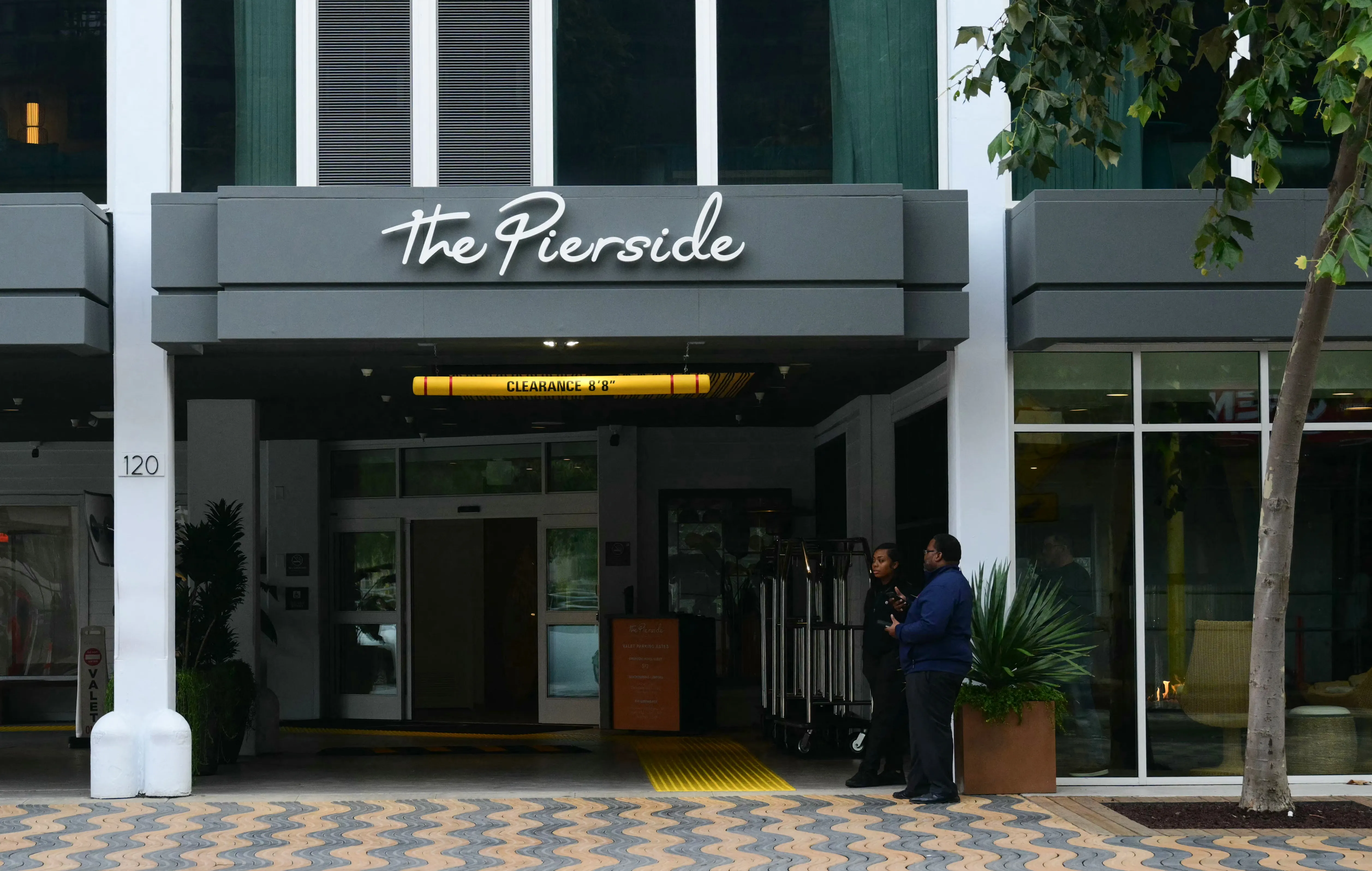 The entrance of The Pierside Santa Monica hotel with two people standing near luggage carts.