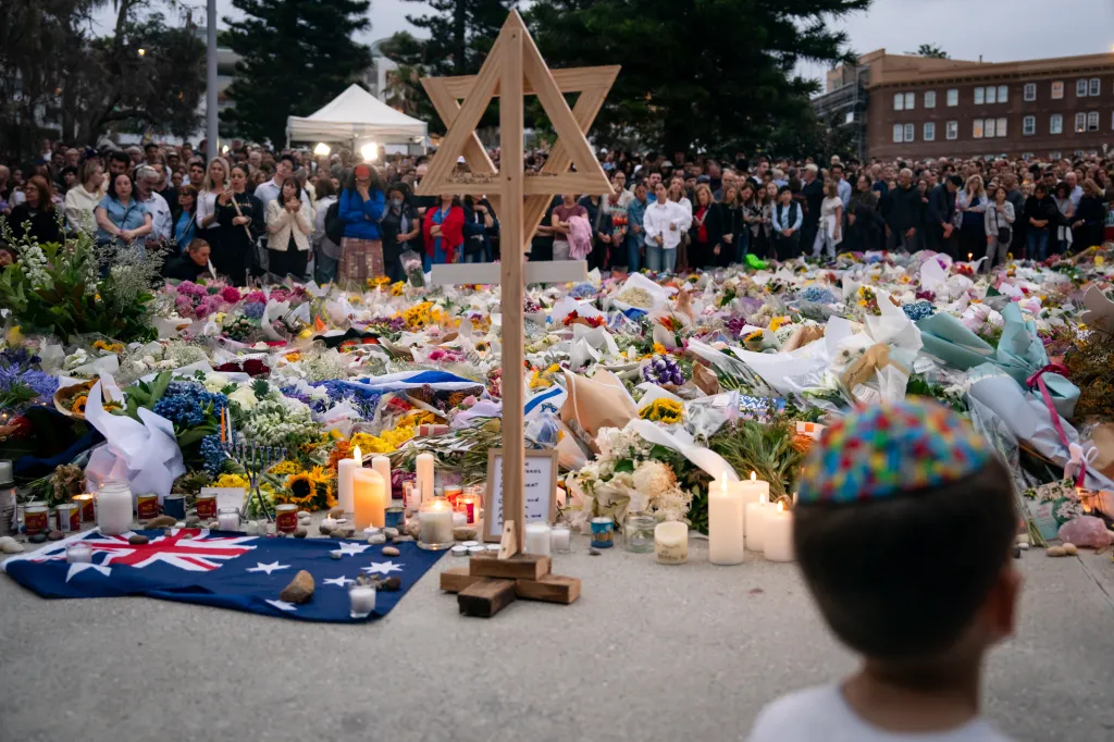 People at a candlelight vigil at Bondi Beach with flowers, candles, and a wooden Star of David.