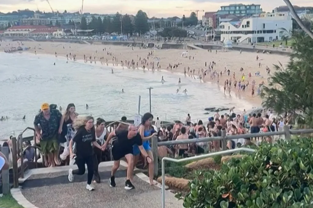 Beach-goers running from the beach and up a ramp as others are in the water and on the sand.