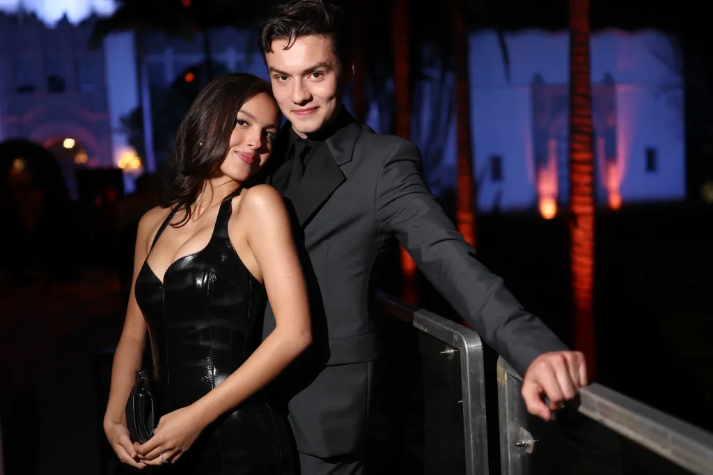 Olivia Rodrigo in a black leather dress and Louis Partridge in a dark suit pose together.