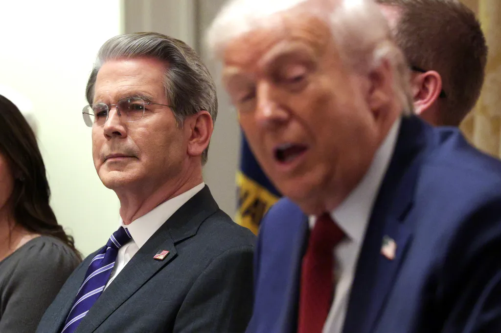U.S. Treasury Secretary Scott Bessent wearing glasses and a blue striped tie, listening as President Donald Trump speaks.