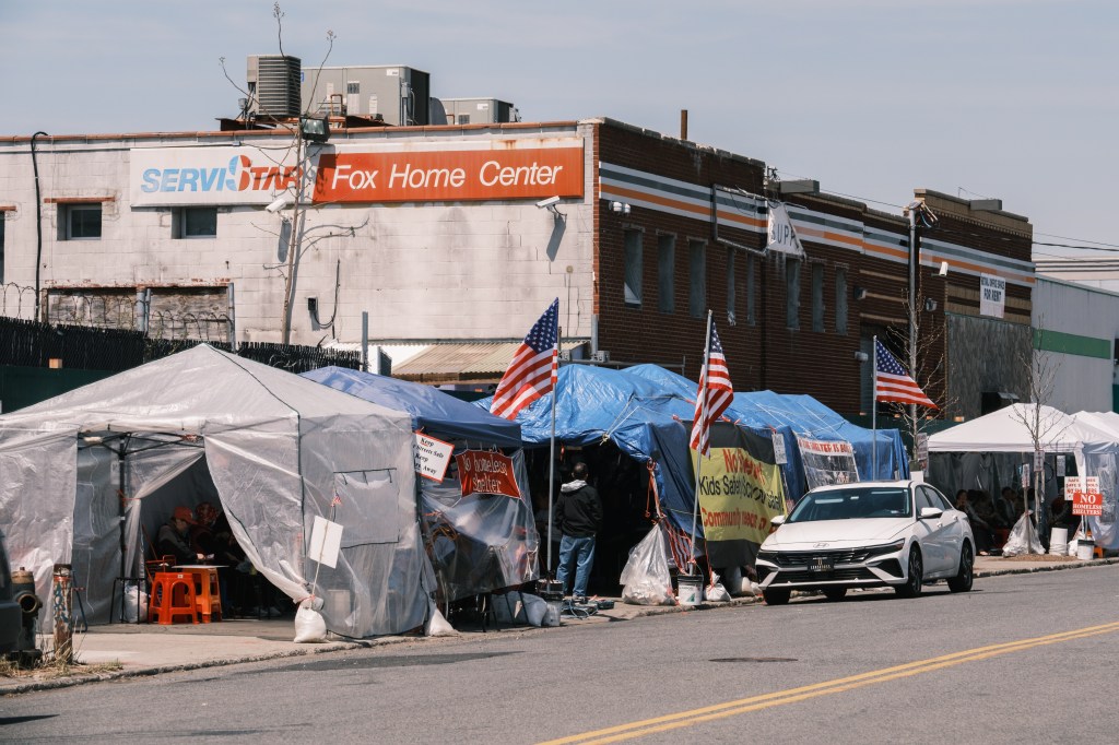 A tent encampment protesting a proposed homeless shelter with signs saying 