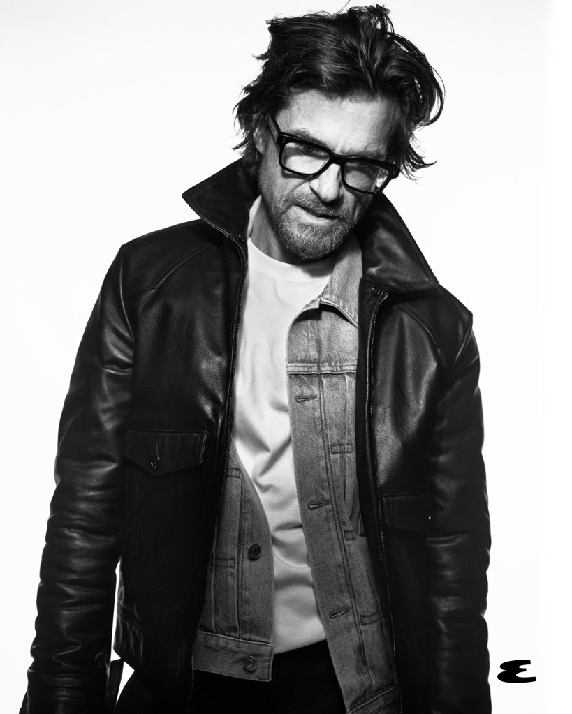 Jason Bateman in a black leather jacket and glasses, looking down and to the left.