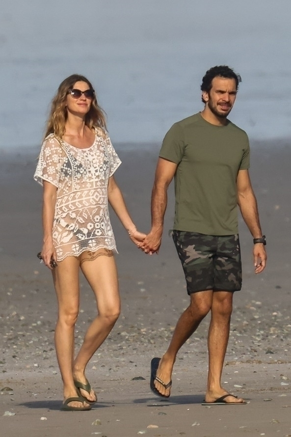 Gisele Bündchen and Joaquim Valente walking hand-in-hand along a beach.