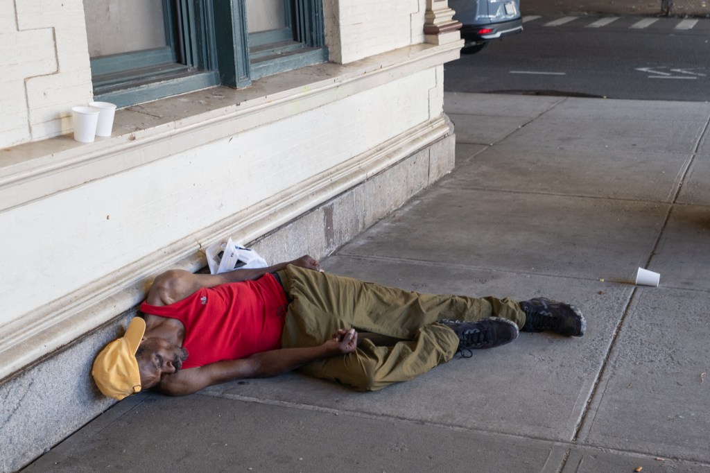 Person sleeping on a sidewalk next to a building.