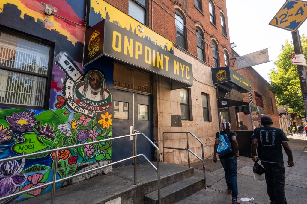 The exterior of OnPoint NYC, with a large colorful mural on the left, a sign for OnPoint NYC, and two people walking towards the entrance.