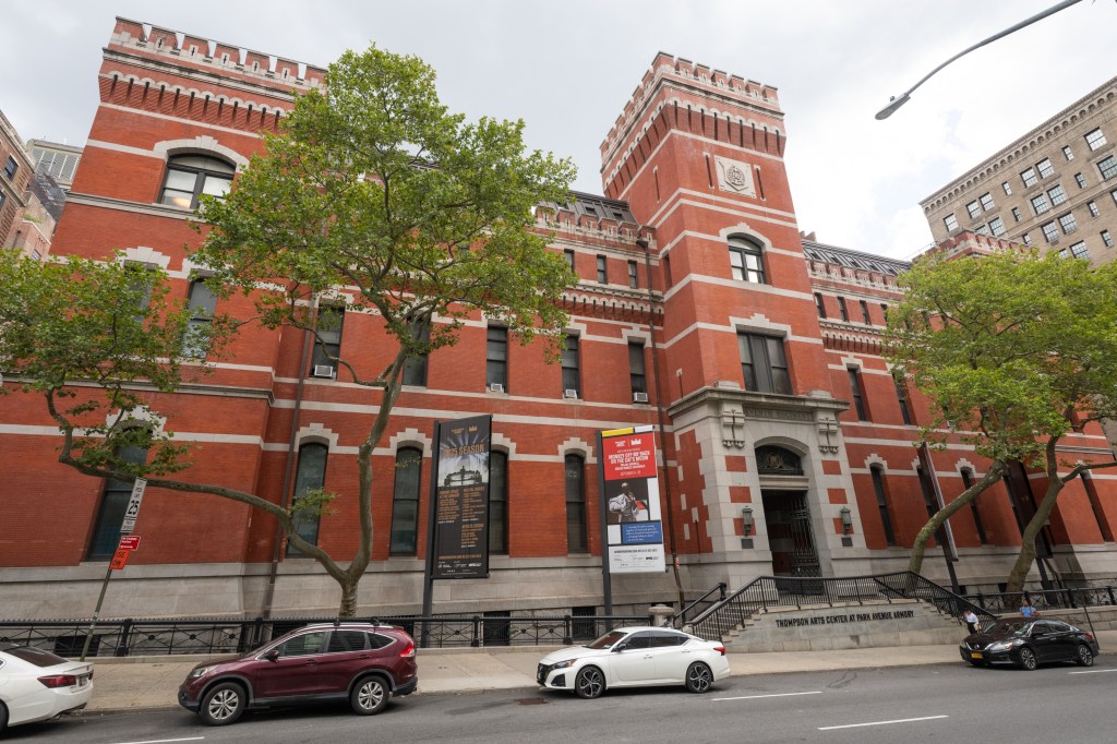 Park Avenue Armory, a red brick building with white trim, is shown from across the street with two large banners for events.