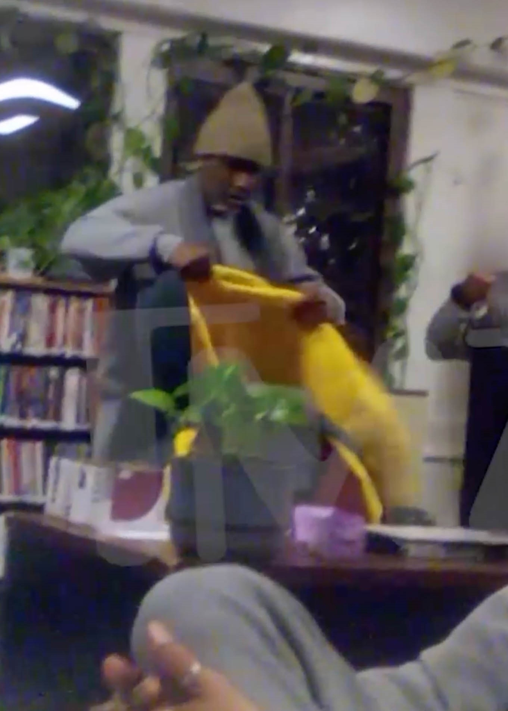 Diddy, wearing a knit cap and gray uniform, takes off a yellow coat in a library.