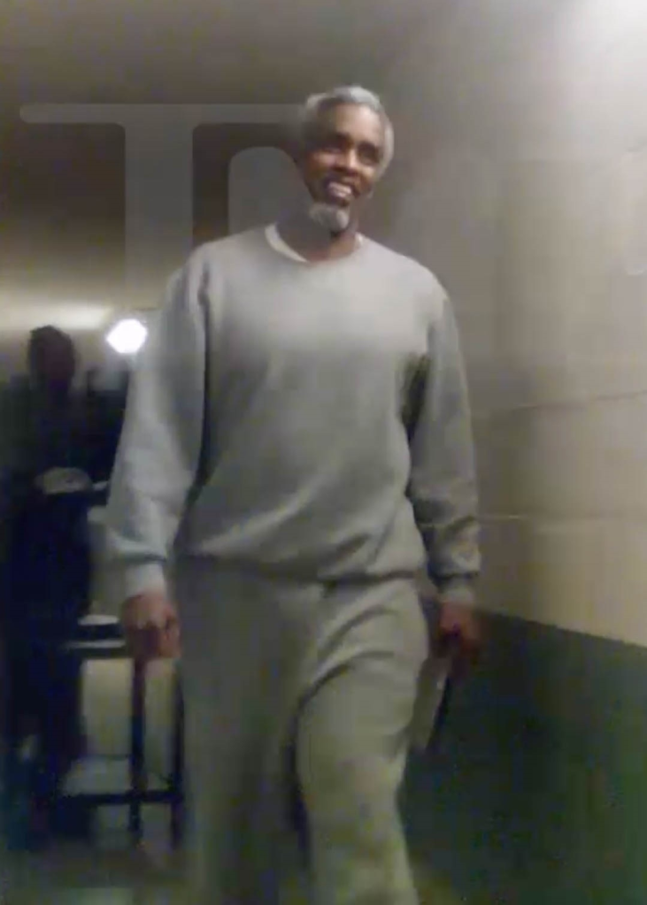 Sean Combs, Diddy, in a gray prison uniform, smiling while walking down a hallway in Fort Dix prison.