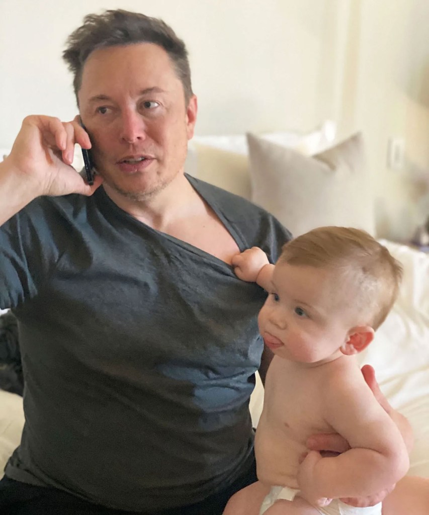 Elon Musk on the phone while holding one of his children.