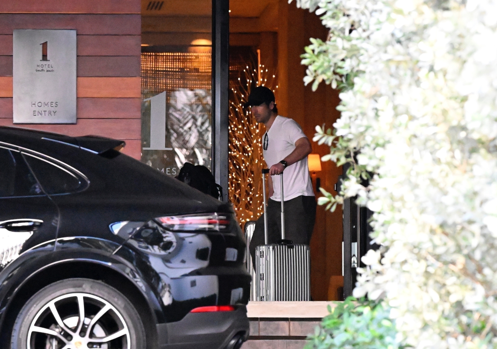 Glen Powell leaving a hotel with luggage in Miami.
