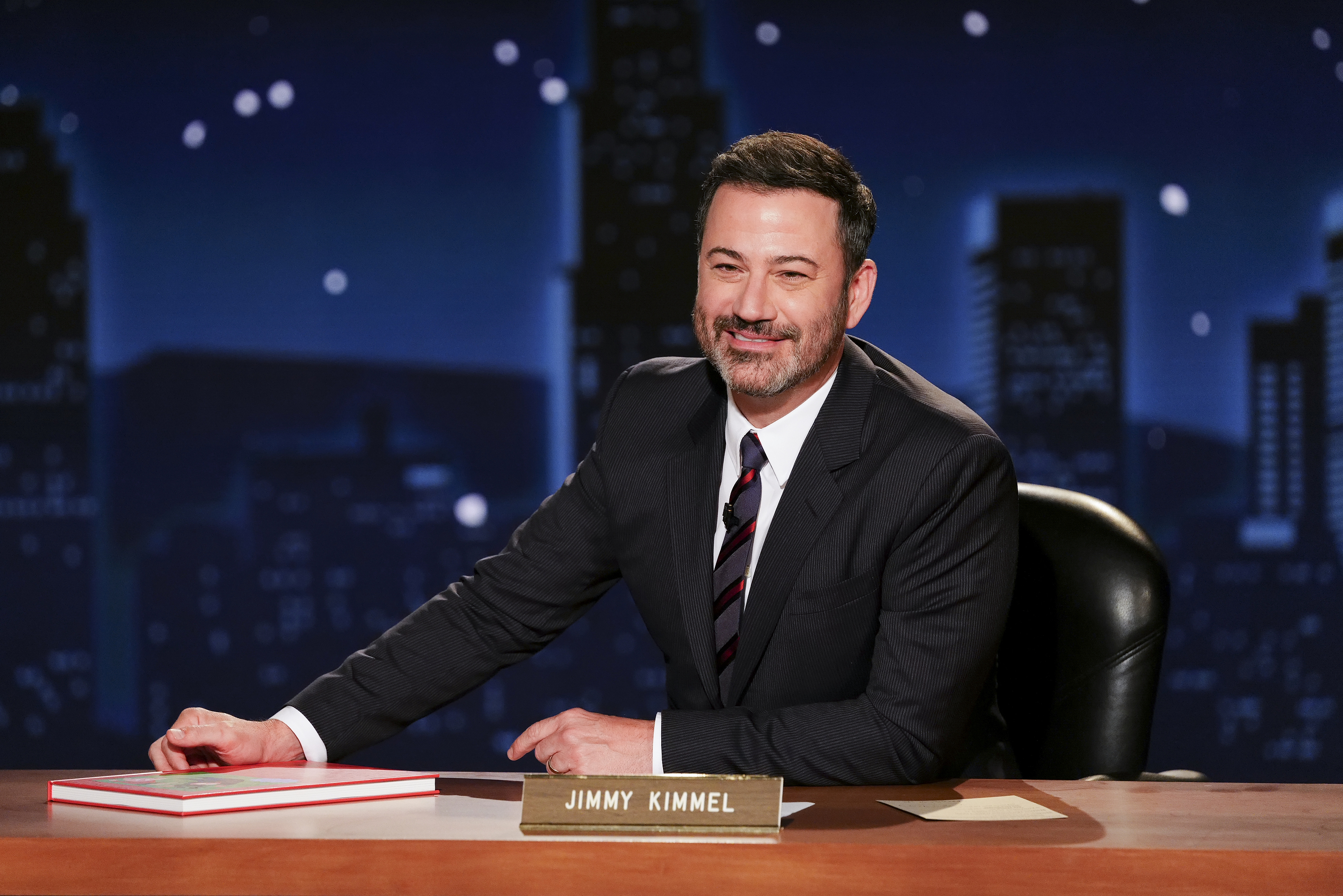 Jimmy Kimmel sitting at his talk show desk.