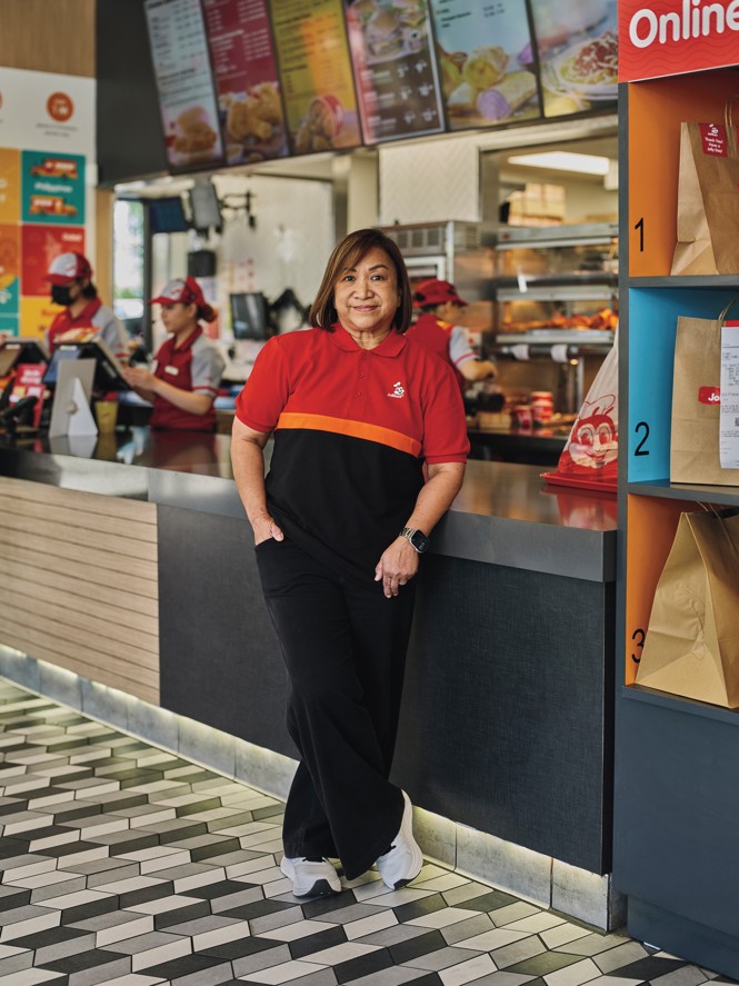 photo of woman in red Jollibee polo and black pants smiling and leaning against brightly colored fast-food counter