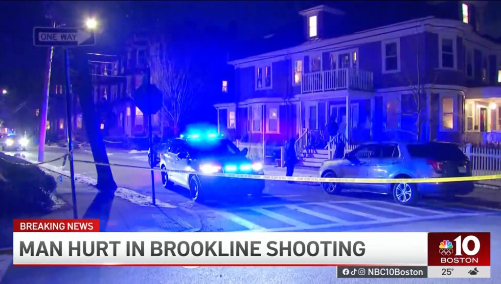Police cars with flashing blue lights and yellow crime scene tape block off a street with houses at night.