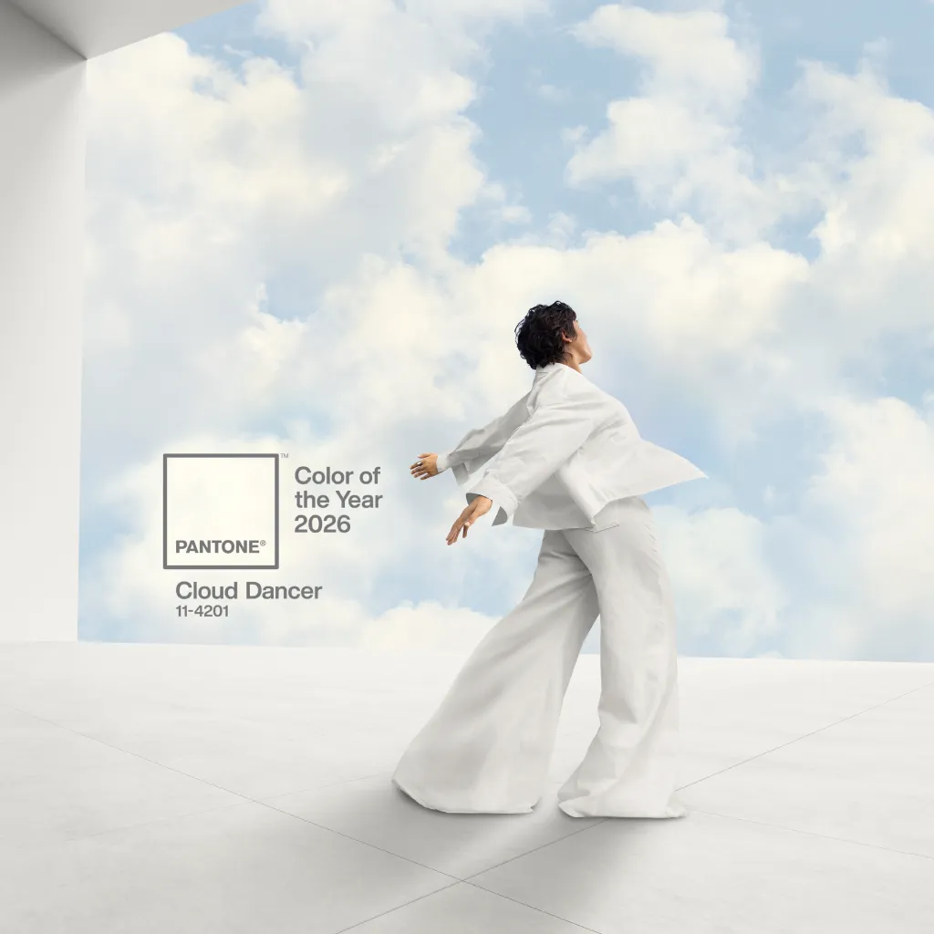 Pantone's Color of the Year 2026, Cloud Dancer, represented by a person in white clothes with arms outstretched against a backdrop of clouds.