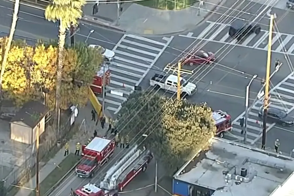 An aerial view of an intersection with emergency vehicles and personnel at the scene of a tree trimming accident.